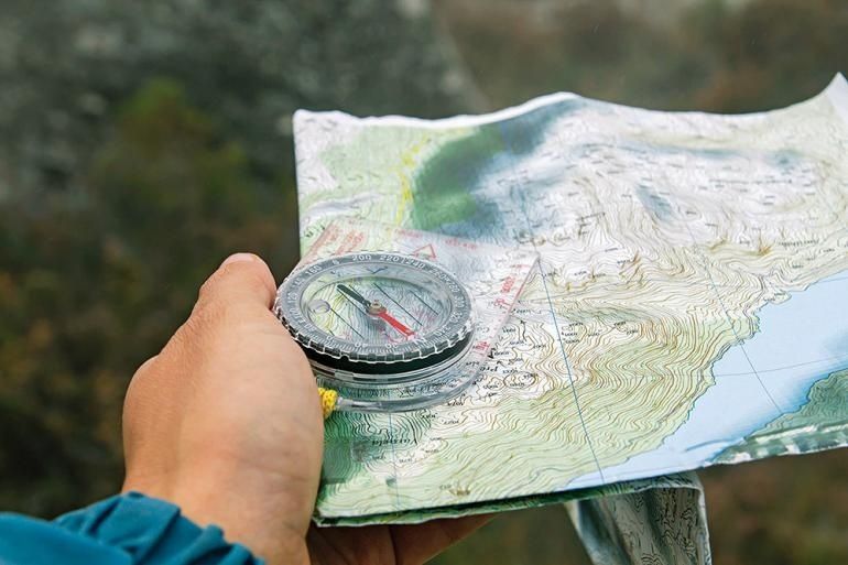 Hand håller en kompass över en topografisk karta i fjällterräng
